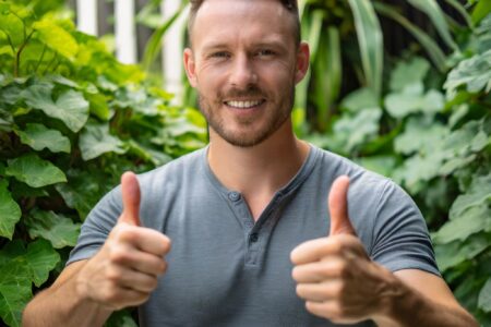 a man in addiction recovery looking calm, cool, and collected, showing two thumbs up and smirking, lush green space